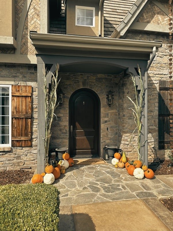 Signature fall porch styling installed at a real customer's home, with cornstalks and layered pumpkins along the walkway.
